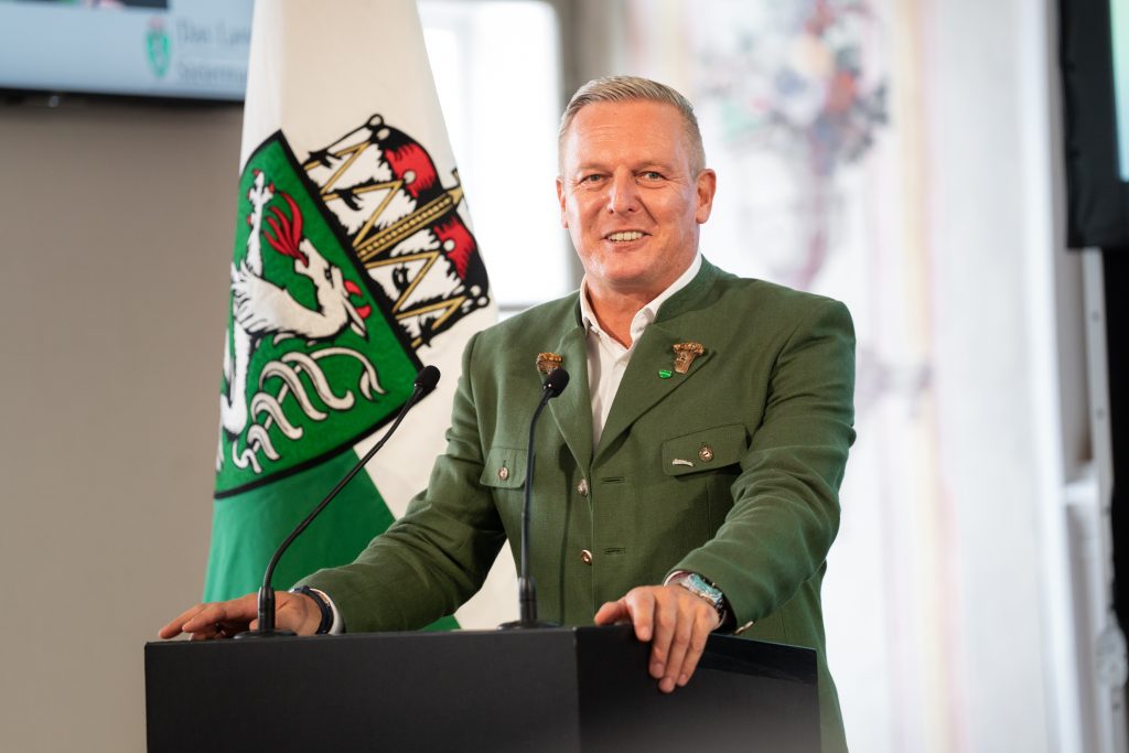 Landeshauptmann Mario Kunasek (FPÖ) im Trachtenanzug am Rednerpult vor einer Steirischen Fahne
